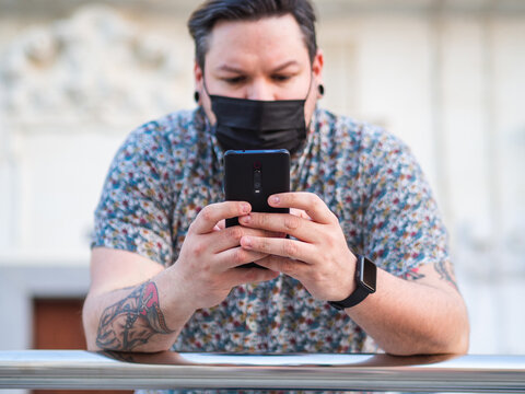 Spanish male with face mask using phone outdoors - concept of the new normal