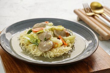 A plate of I Fu Mie or Crispy Fried Noodle with thick savory sauce and meatball and vegetables in shiny and grainy white background. Selective focus