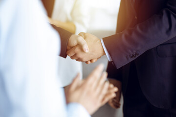 Unknown businesspeople are shaking their hands after signing a contract, while standing together in a sunny modern office, close-up. Business communication concept