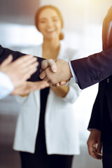 Unknown businesspeople are shaking their hands after signing a contract, while standing together in a sunny modern office, close-up. Business communication concept