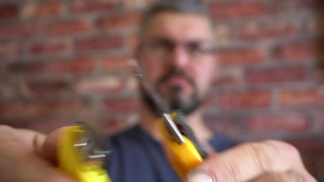 A Man Holds Two Office Knives In His Hands. Yellow Handles. Blurred Face On The Background. Close-up.