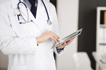 Unknown male doctor using tablet computer in clinic near his working place, closeup. Perfect medical service in hospital. Medicine and healthcare concept