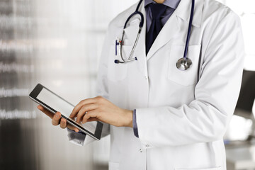 Unknown male doctor using tablet computer in clinic near his working place, closeup. Perfect medical service in hospital. Medicine and healthcare concept