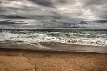 Brave ocean, rock formations and cloudy drama sky on the beach