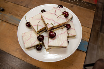 A delicious plate of Cherry Bakewell Squares Tarts on a wooden kitchen table surrounded by cherries
