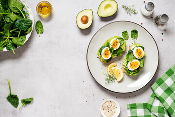 Healthy toast with sliced avocado, boiled eggs, spices and fresh spinach. Delicious breakfast or snack on gray stone background. top view, space for text
