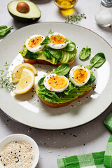 Healthy toast with sliced avocado, boiled eggs, spices and fresh spinach. Delicious breakfast or snack on gray stone background.