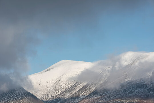 Epic landscape image of Skiddaw snow capped mountain range in Lake District in Winter with low level cloud around peaks viewed from Derwentwater