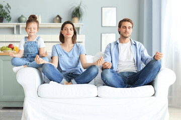 Calm young family with little daughter sit on couch practice yoga together, happy parents with...