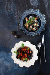 Mussels in cream sauce. Mussels in tomato sauce with hot red pepper. Seafood on plate. Two dishes in stylish ceramic dishes. Top view. Blue textured background. Vertical photo.Free space.