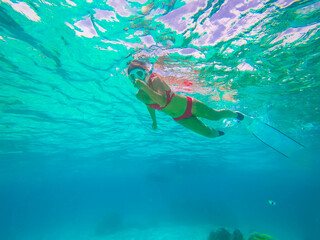 Young woman in red bikini Freediver gliding underwater over vivid coral reef