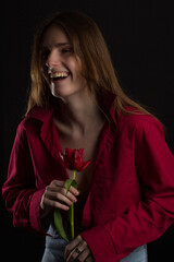 Studio portrait of a young woman on a black background with bouquet of red tulips in her hands