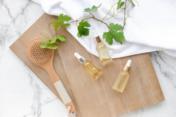 Bottles of grape seed oil with massage brush and towel on white background