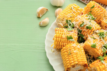 Plate with tasty baked corn cobs on color wooden background