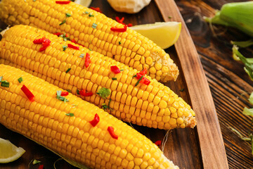 Board with tasty baked corn cobs on wooden background