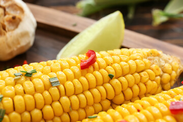 Board with tasty baked corn cobs on wooden background, closeup