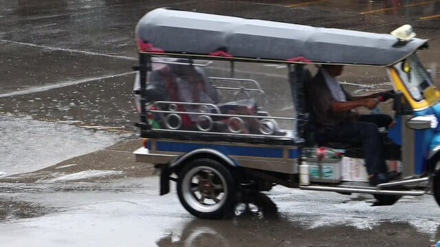 The traditional motor tricycle - tuk tuk, rides with a passenger in the rain.