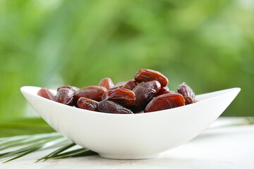 Bowl with sweet dried dates on table against blurred background