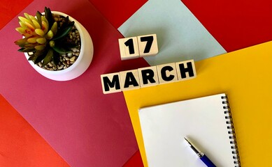 March 17 on wooden cubes. Next to it is a white notebook, a pen, and a potted flower .Calendar for March.