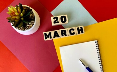 March 20 on wooden cubes. Next to it is a white notebook, a pen, and a potted flower .Calendar for March.