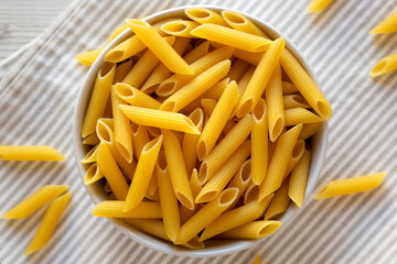 Uncooked Organic Penne Pasta in a Bowl, overhead view. Flat lay, top view, from above. Close-up.