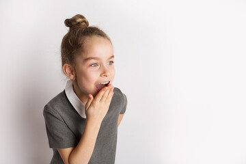 Attractive little girl in a strict school dress, stands on a white background with empty copy space, gestures with her hands, admires a happy expression on her face