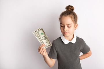 Attractive little girl in a strict school dress, stands on a white background with empty copy space, gestures with her hands, admires a happy expression on her face