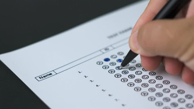 Education and exam concept. Answering multiple-choice test questions. A student filling out test sheet. Student hand with pen fill in exam test answer sheet. Answering test questions on the exam