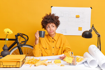 Skilled professional female engineer drinks coffee prepares drawings for house development project...