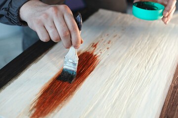 A working cabinetmaker holds a brush in his hand and paints a wooden surface. A trace of paint on a...