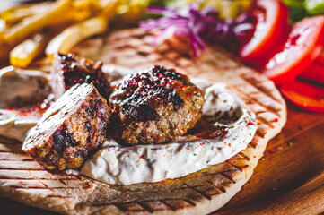 Spicy bifteki, frikadelle or frikkadel meatballs with minced beef and lamb with pita bread, tzatziki dip, vegetables salad and French fries. Greek meatballs keftedes or Keftedakia.