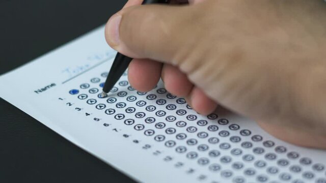 Education and exam concept. Answering multiple-choice test questions. A student filling out test sheet. Student hand with pen fill in exam test answer sheet. Answering test questions on the exam