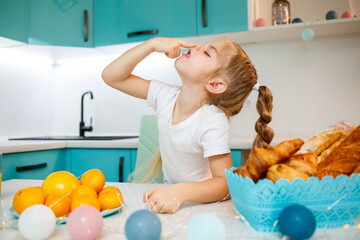Close up portrait of a little girl of seven years old. Fooling around sitting at the table in the kitchen. Dressed in a white t-shirt