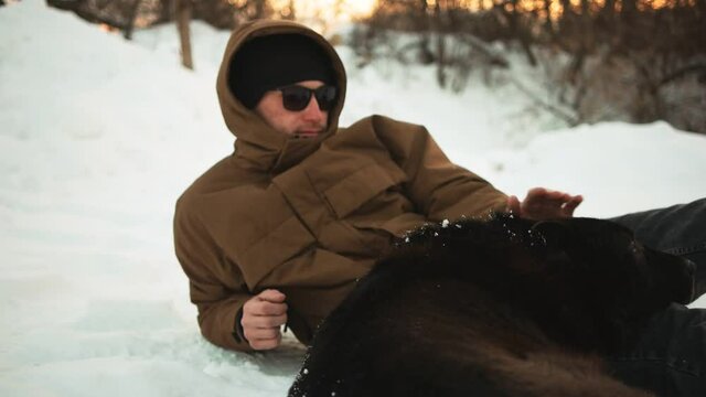 A young guy is stroking his dog. On open air. Winer.