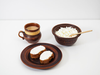 A cup of aromatic coffee with milk, a plate with baguette and cottage cheese sandwiches, a bowl with farm cottage cheese on a white background. Handmade earthenware with birch bark decoration. Pottery