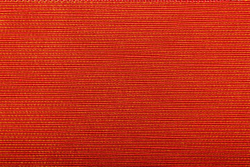 Fototapeta premium Factory fabric of red color with yellow threads interspersed. Close-up long and wide texture of natural red fabric. Fabric texture of natural cotton or linen textile material. Red canvas background