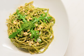 Mediterranean spaghetti with basil arugula pesto decorated with roasted pine nuts and fresh rocket salad
