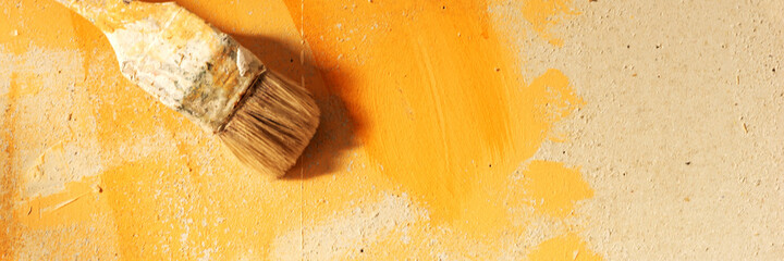 Paintbrush in front of the orange color wall. Panoramic image