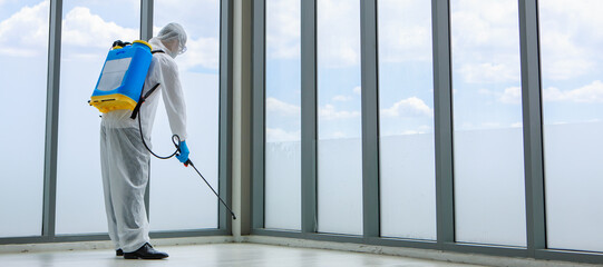 Officer wearing sterilize protective suit with chemical tank on back spraying Disinfectant solution in office place to reduce and protect coronavirus