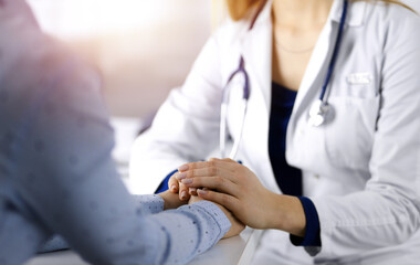 Unknown woman-doctor is holding her patient's hands to reassure the patient, discussing current...