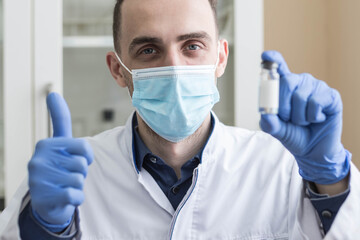 A young doctor in a medical mask holds an ampoule of liquid in his hand and shows the class. The concept of healthcare and medicine.