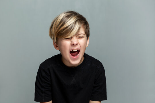 A 9-year-old boy in a black T-shirt shouts. Depression, loneliness and learning difficulties. Grey background.