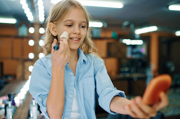 Little girl holds brush at mirror in makeup salon