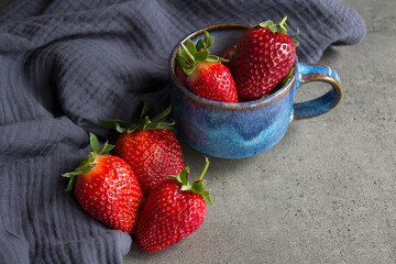 Juicy strawberries on blue ceramic plate. Fresh berries close up photo. Grey textured background. 