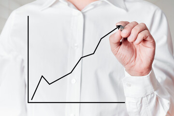 Businessman with pen draws a rising line graph on virtual screen.