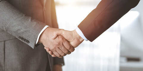 Business people standing and shaking hands in sunny office, close-up. Handshake and marketing