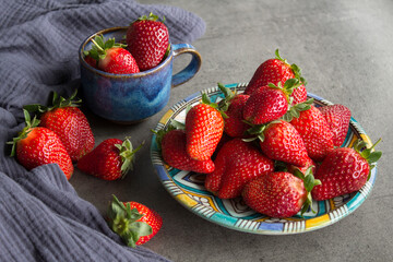 Fruit diet concept. Blue ceramic plate and cup full of fresh juicy strawberries on a table. Dark gray textured background. Eating fresh concept. 
