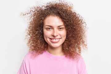 Portrait of good looking curly woman smiles toothily happy to hear good news spends free time with friends dressed in casual jumper isolated over white background. People and emotions concept