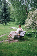 Fototapeta premium Portrait of beautiful caucasian woman in long white retro dress walking in green summer blossom park on meadow. Rays of sunlight. Lady girl. Book cover