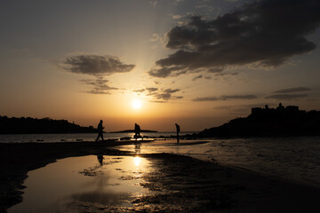 Three people's silhouette at the beach with the sunset at background